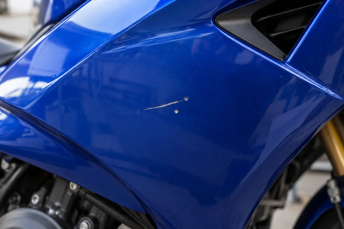 Illustration générée : petite rayure et éclats sur un carénage de moto bleu sans marque, avant retouche.
